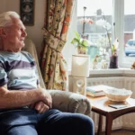 Elderly man looking out window symbolizing loneliness